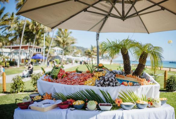 A seafood buffet, loaded with fresh oysters, prawns and more sits under a large umbrella near the beach © Tangalooma Island Resort