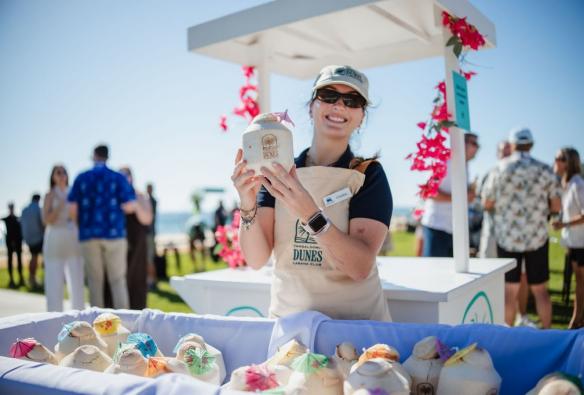 A staff member wearing a hat and sunglasses working at a drinks stand holding up a coconut © Tangalooma Island Resort
