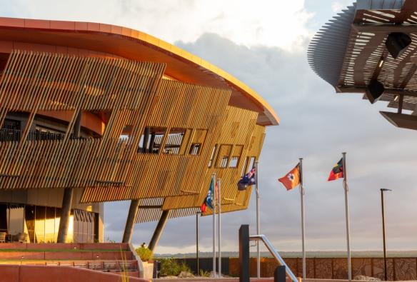 A new building with timber battens as the cladding sits lit by afternoon sun, right by the harbour. © Larrakia Cultural Centre