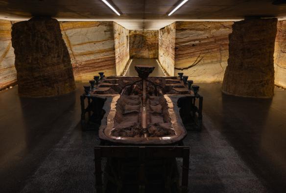 A cast copper and iron installation artwork sits in a museum room lined with sandstone walls and low concrete ceilings. © MONA/Jesse Hunniford