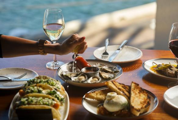 A close up of a hand squeezing lemon over half a dozen oysters. © The Oriana / Steven Woodburn