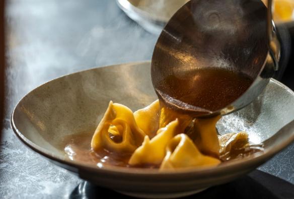 Broth is ladled over a steaming plate of handmade tortellini. © Andrew Wilson Photography